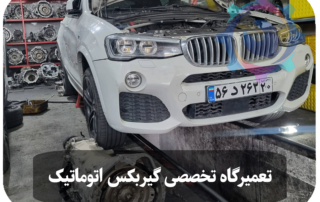 خودروی BMW X4 سفید رنگ که در حال تعمیر گیربکس اتوماتیک در تعمیرگاه تخصصی تویوکارا است. گیربکس جدا شده و در کنار خودرو قرار دارد، در حالی که خودرو روی بالابر قرار گرفته است.